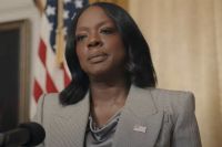 Viola Davis wearing a gray pantsuit, in front of a U.S. flag, in the role of the U.S. President, in the movie G20.