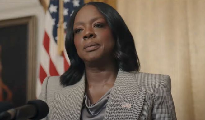 Viola Davis wearing a gray pantsuit, in front of a U.S. flag, in the role of the U.S. President, in the movie G20.
